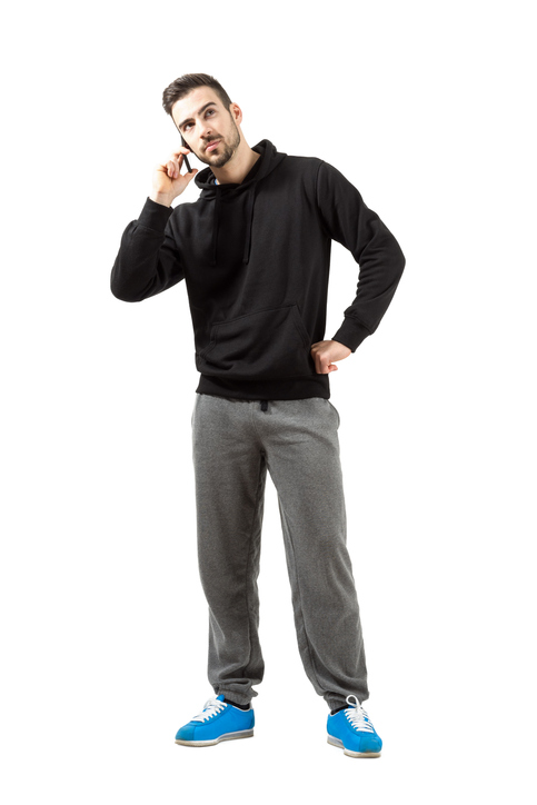 Young man in hood and sweatpants talking on mobile phone.  Full body length isolated over white background.